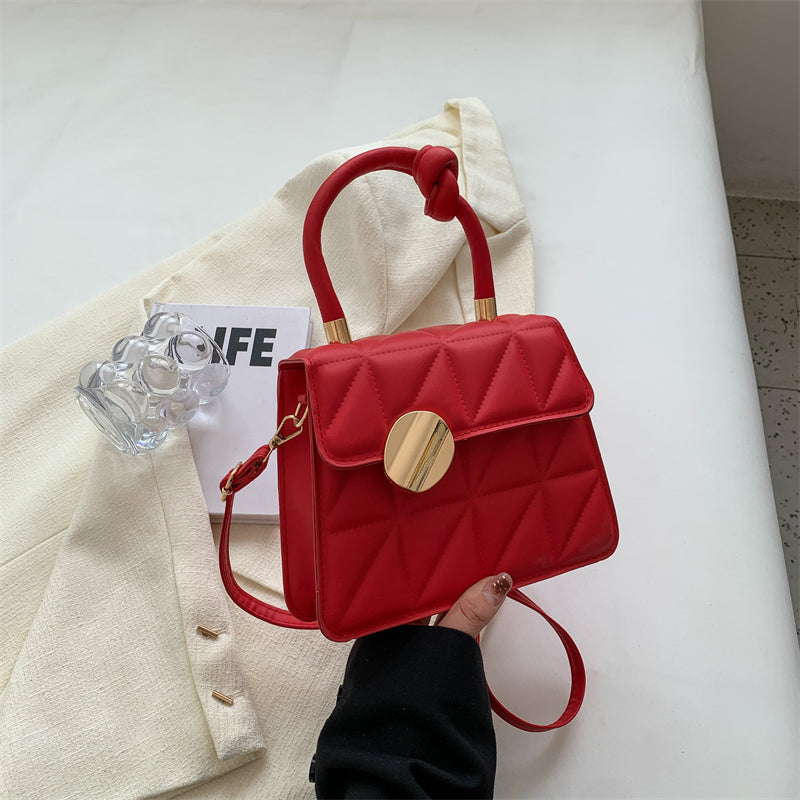 Red handbag with gold accents held by a hand on a light background