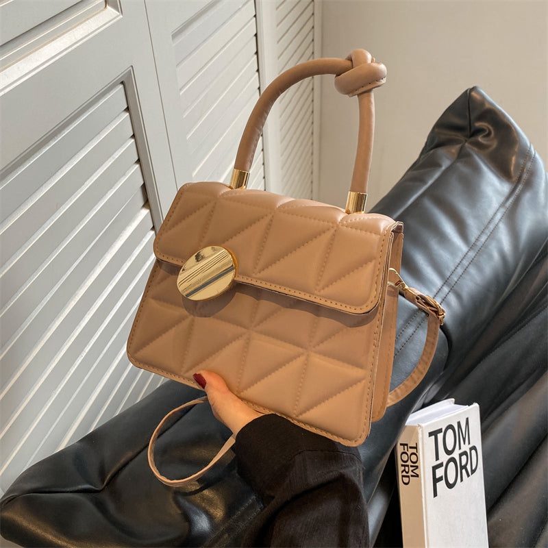 Beige quilted handbag held by a person with a blurred background