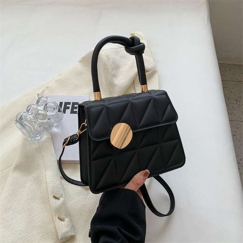 Black handbag with gold accents held by a hand on a white surface.