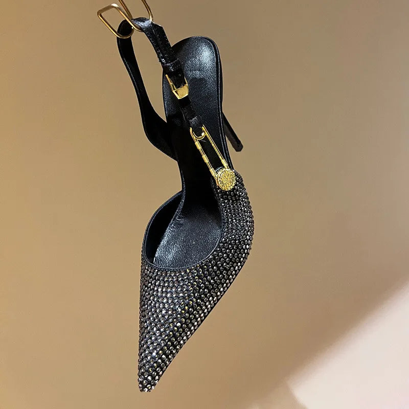 Black studded high-heeled shoe with gold accents on a beige background