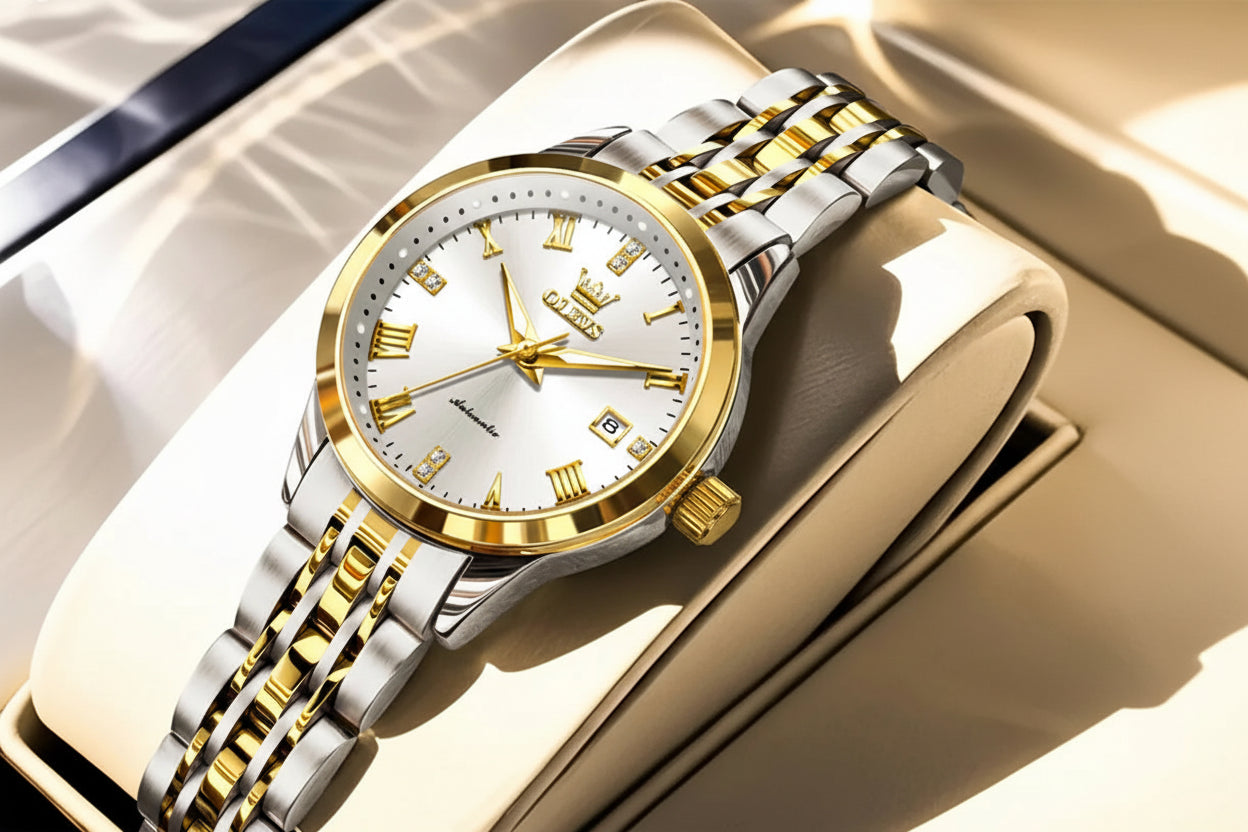 Gold and silver watch with white face on a reflective surface, OLEVS brand visible.