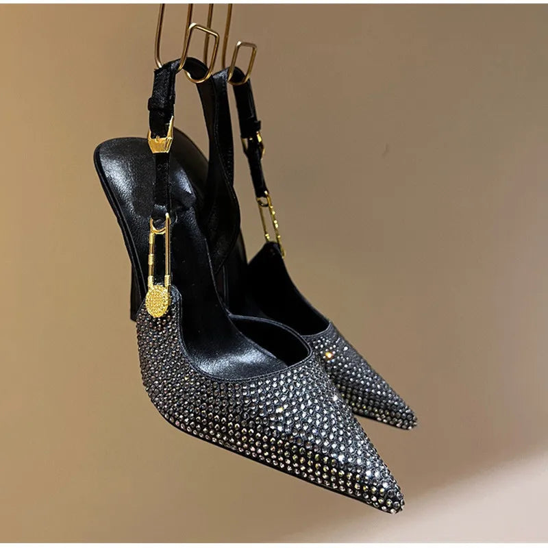 Black studded high-heeled shoes with gold accents on a beige background
