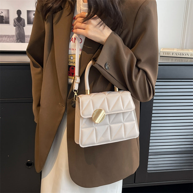 Person wearing a brown coat holding a white quilted handbag with gold accents.