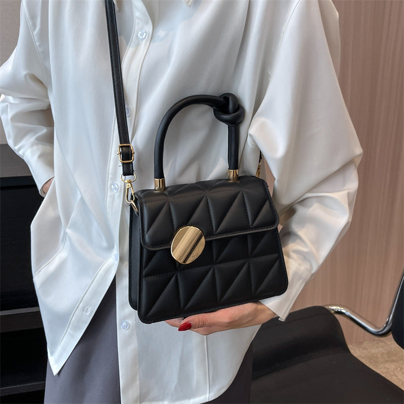 Person holding a black quilted handbag with gold accents